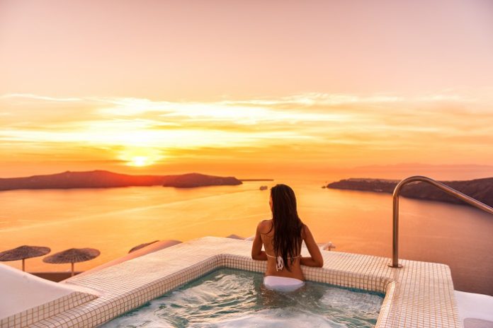 Luxury travel Santorini vacation woman swimming in hotel jacuzzi pool watching sunset. Europe resort destination holiday for honeymoon getaway.