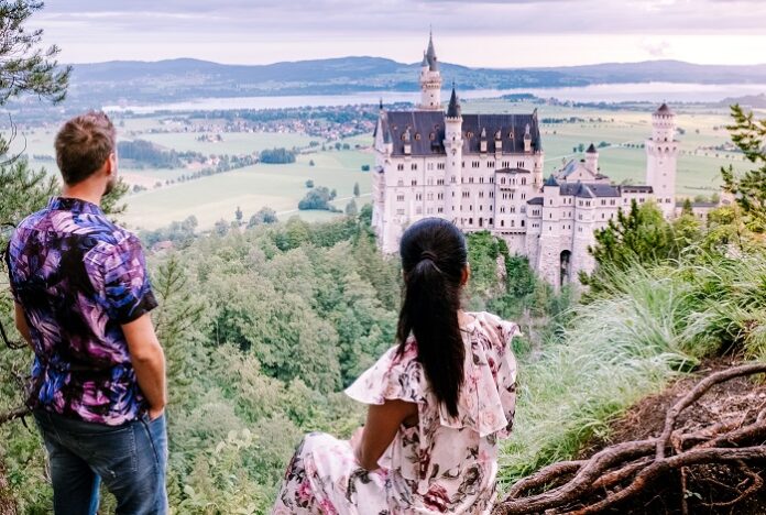 couple men and woman visit Neuschwanstein Castle. Beautiful view of world-famous Neuschwanstein Castle, the nineteenth-century Romanesque Revival palace built for King Ludwig II on a rugged cliff near Fussen, southwest Bavaria, Germany Turistleri Yamaçtan İten Amerikalıya Ömür Boyu Hapis Cezası