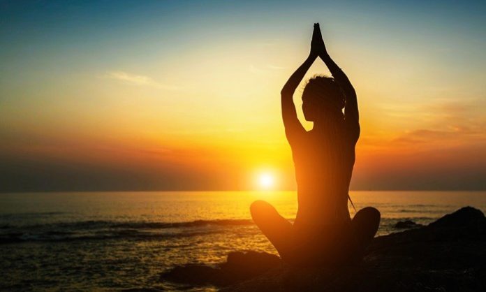 Yoga woman silhouette. Meditation on the ocean during amazing sunset.